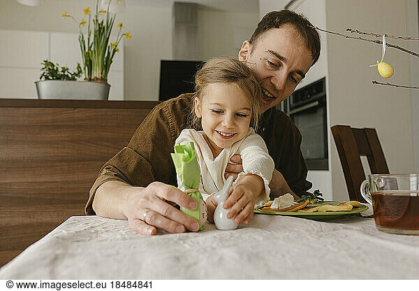 Father and daughter playing with Easter egg and bunny at table at home