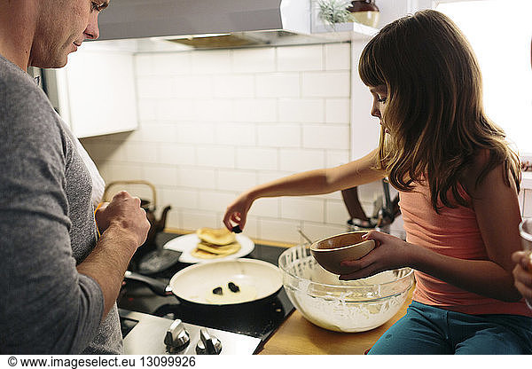 Father and daughter preparing food in kitchen at home