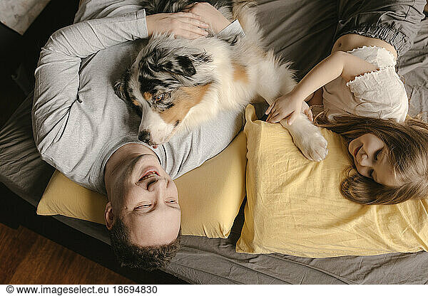 Father and daughter relaxing with Australian Shepherd on bed at home
