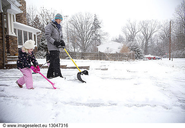 Father and daughter removing snow with shovels in backyard