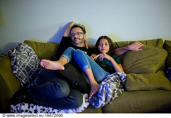 Father and daughter snuggle on couch and watch tv