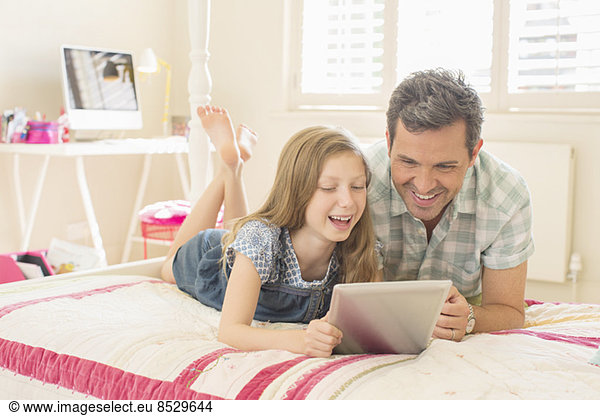 Father and daughter using digital tablet on bed