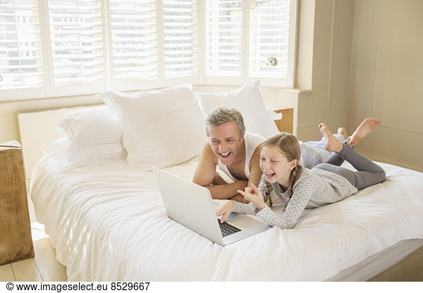 Father and daughter using laptop on bed