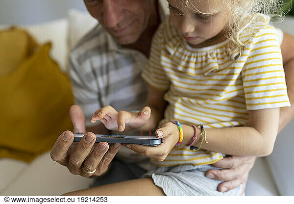 Father and daughter using mobile phone together at home