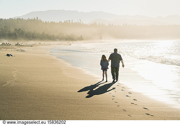 Father and daughter walking along beach at sunset