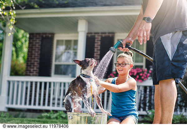 Father and daughter washing dog with hosepipe