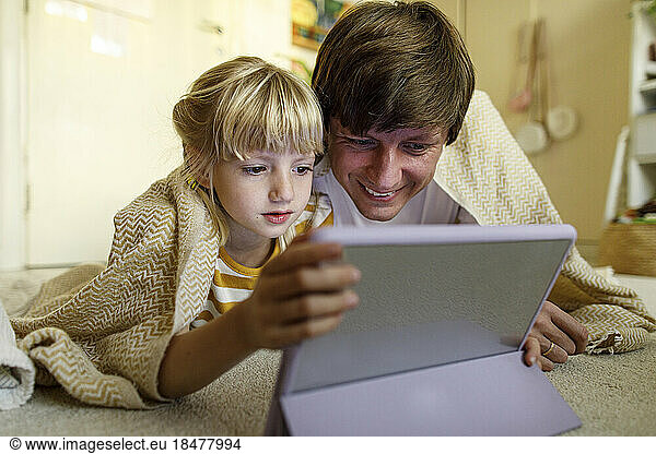 Father and daughter watching tablet PC lying on floor at home