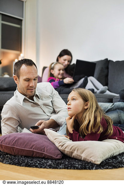 Father and daughter watching TV on floor with family in background