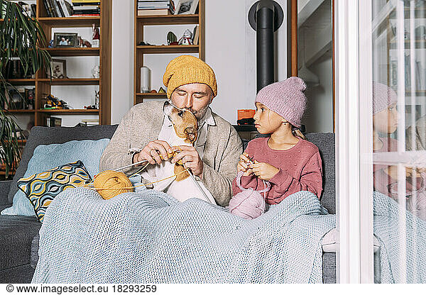 Father and daughter with dog knitting on couch at home together
