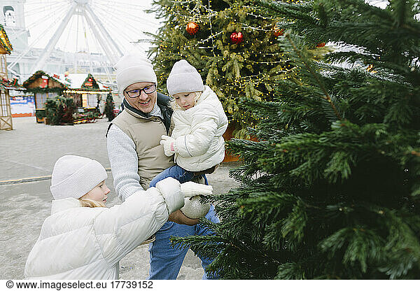 Father and daughters putting Christmas ornament on tree in market