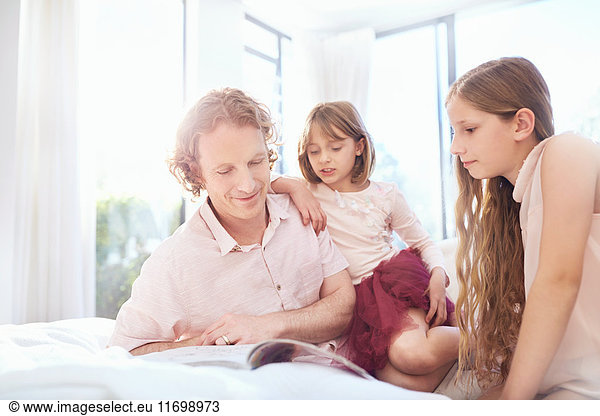 Father and daughters reading book on bed