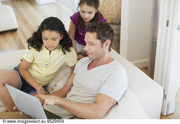 Father and daughters using laptop on sofa in living room