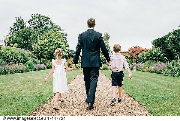 father and kids dressed for a wedding walking in a beautiful garden