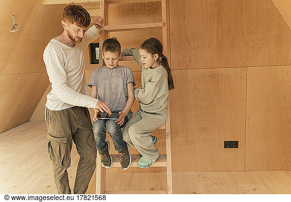 Father and kids using tablet pc at wooden eco house