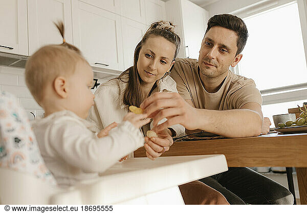 Father and mother feeding fruit to daughter sitting at home