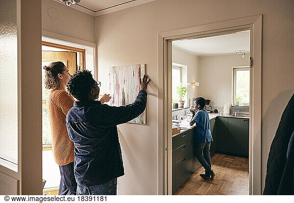 Father and mother hanging painting on wall with son standing in kitchen at home