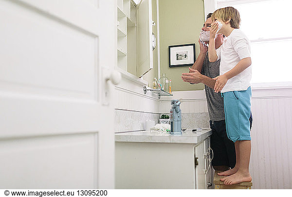Father and son applying shaving cream on face in bathroom