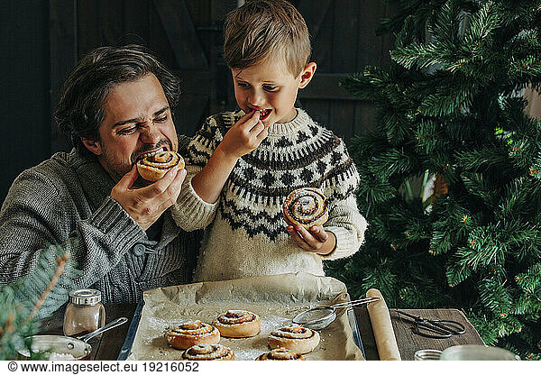 Father and son eating cinnamon buns at table