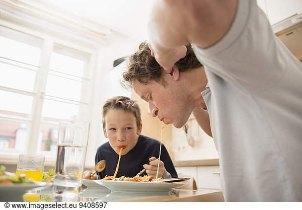 Father and son eating spaghetti in kitchen