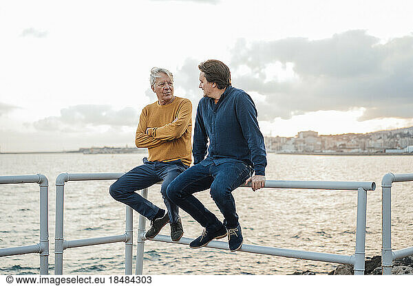 Father and son having discussion together sitting on railing