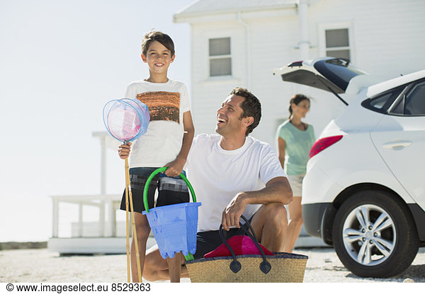 Father and son holding beach gear outside car in sunny driveway