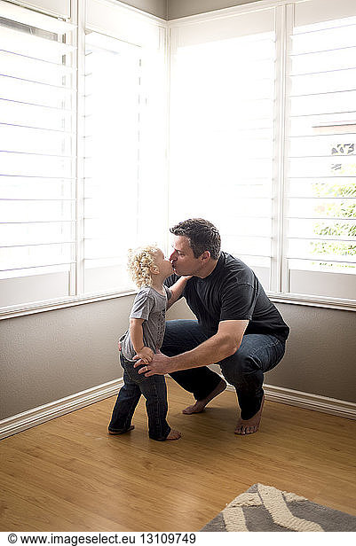 Father and son kissing on mouth against windows at home