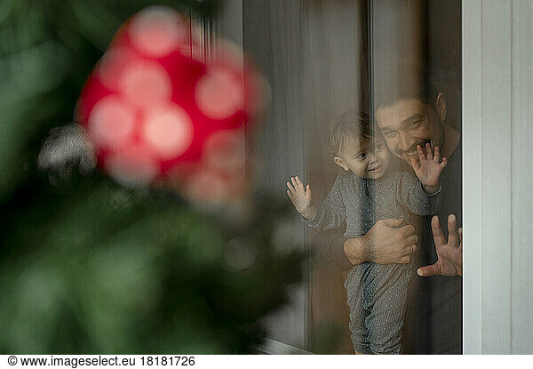Father and son looking out of window at Christmas tree in home