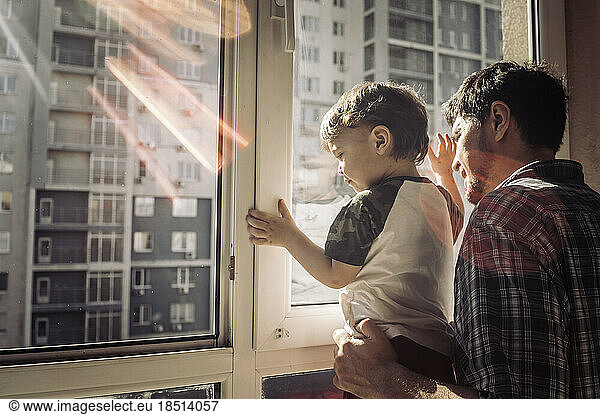 Father and son looking out of window at home