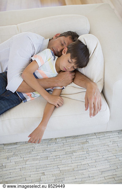 Father and son napping on sofa in living room