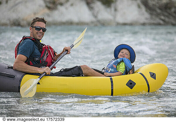 Father and son paddle river on a packraft  wearing lifejackets.