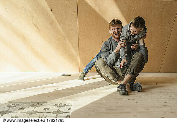 Father and son play fighing on the floor in wooden eco house