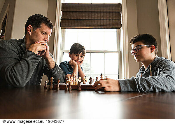Father and son playing chess at a table while little brother watches.