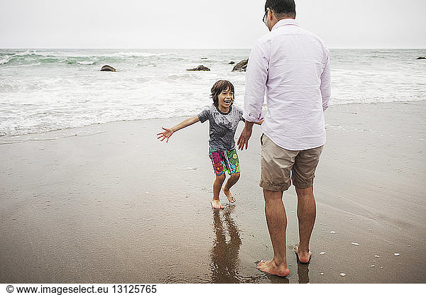 Father and son playing on wet sand at shore
