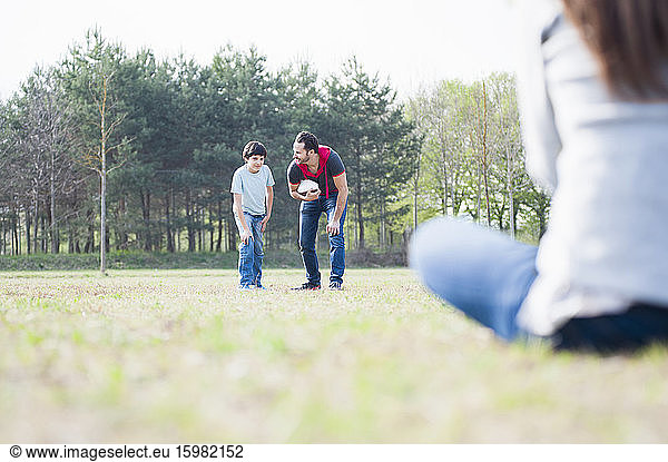 Father and son playing rugby with woman in park