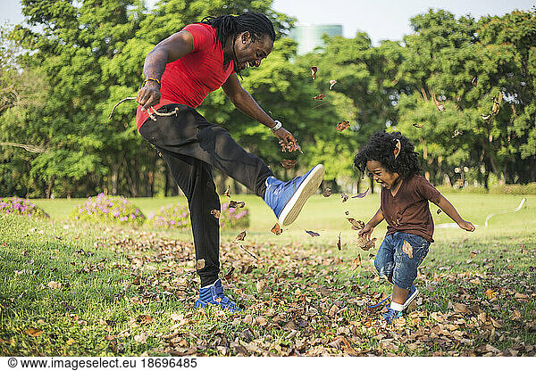 Father and son playing with dried leaves at park