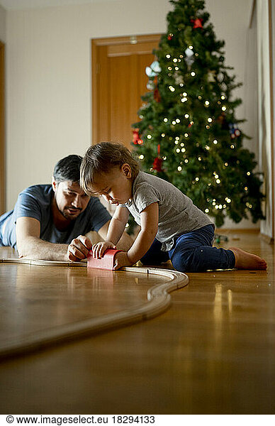 Father and son playing with wooden toy train in front of Christmas tree at home