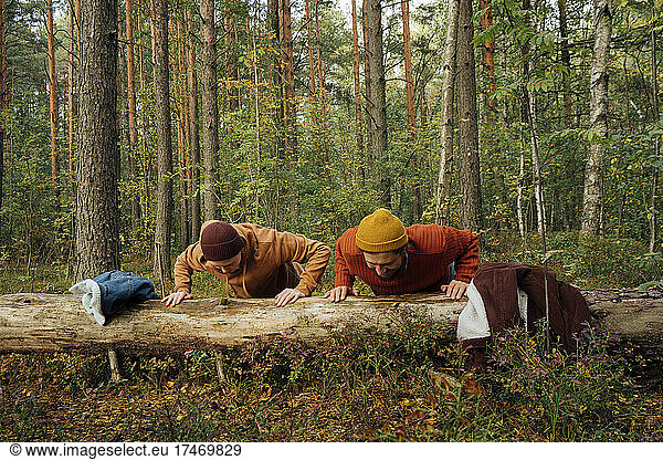 Father and son practicing push-ups on tree log in forest