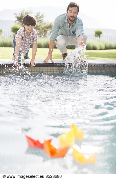 Father and son racing paper boats in swimming pool
