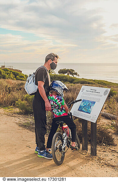 Father and son reading a sign at a trail  son riding a bike.