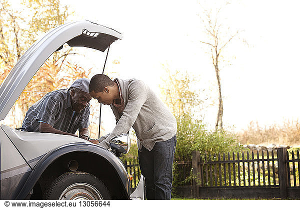 Father and son repairing car against sky