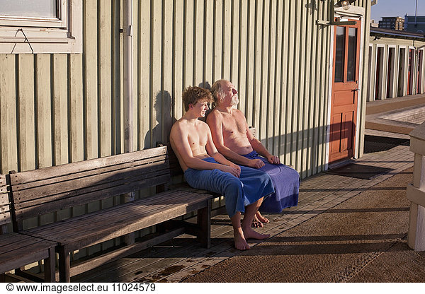 Father and son resting on bench against beach hut