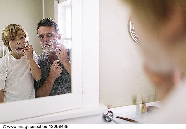 Father and son shaving while reflecting in mirror