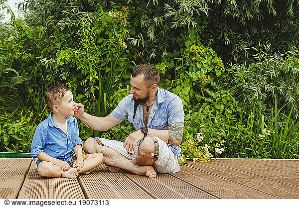 Father and son sitting on footbridge in front of plants