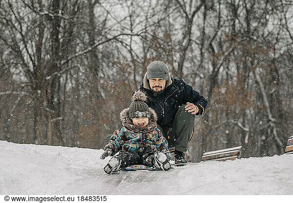 Father and son sledding down on snowy hill