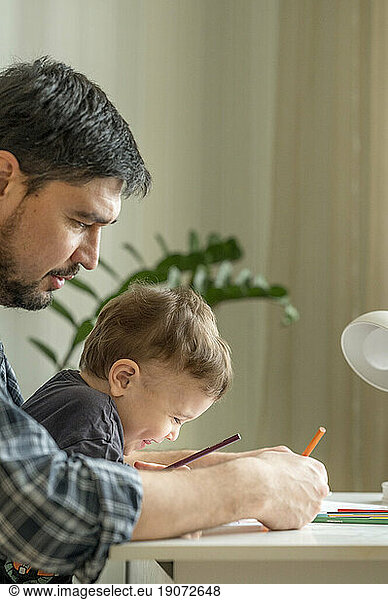 Father and son spending leisure time doing coloring at home