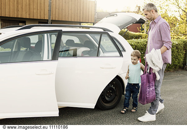 Father and son standing by car with open doors and trunk on street