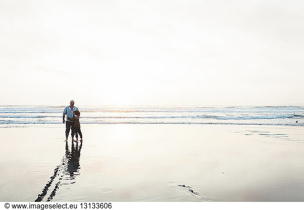 Father and son standing on shore at beach against clear sky