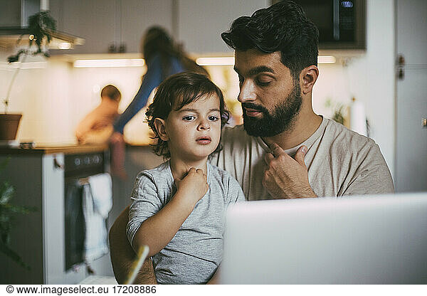 Father and son taking online advice through laptop at home
