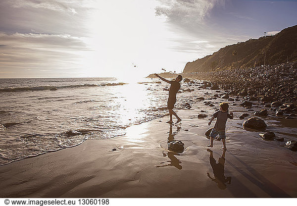 Father and son throwing stones in sea during sunset