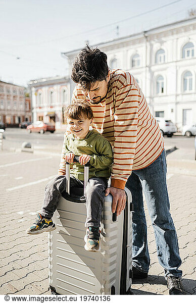 Father and son traveling together with suitcase on sunny day